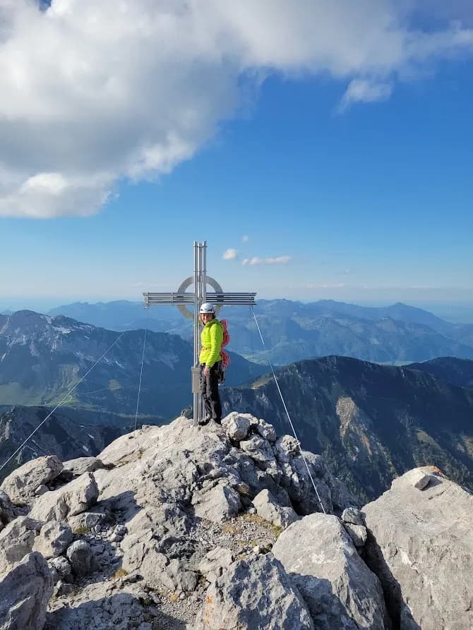 Glücklicher Kletterer am Gipfel Kreuz der Fleischbank nach einem geglückten Aufstieg über den Nordgrat mit Bergführer